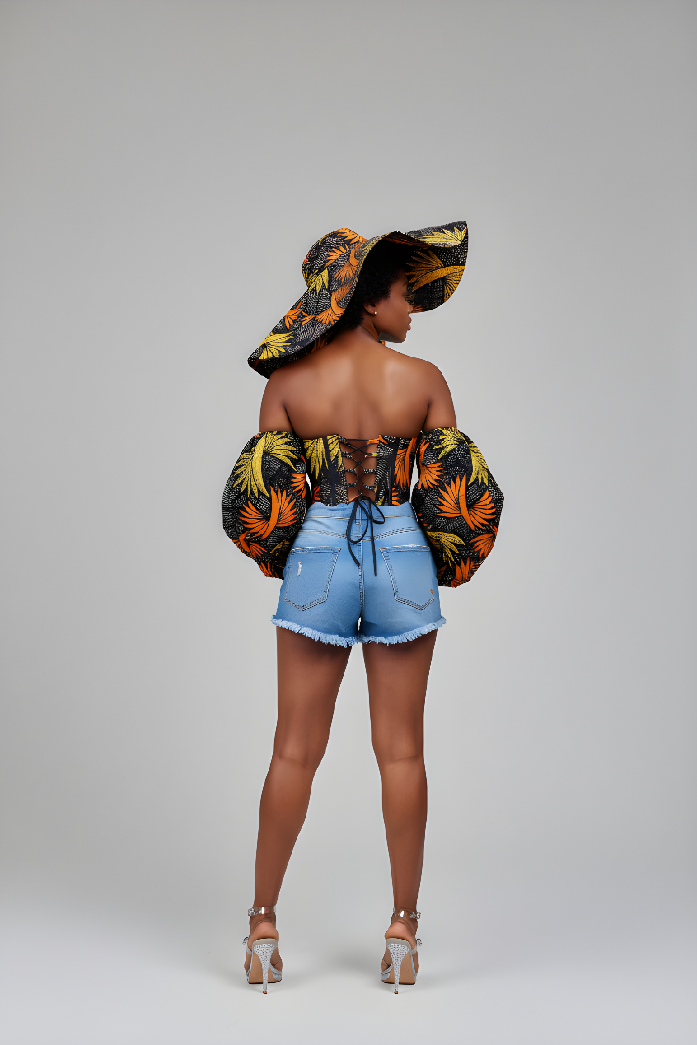 Ankara corset top with puff sleeves and matching wide-brim hat styled with distressed denim shorts and sneakers. 
