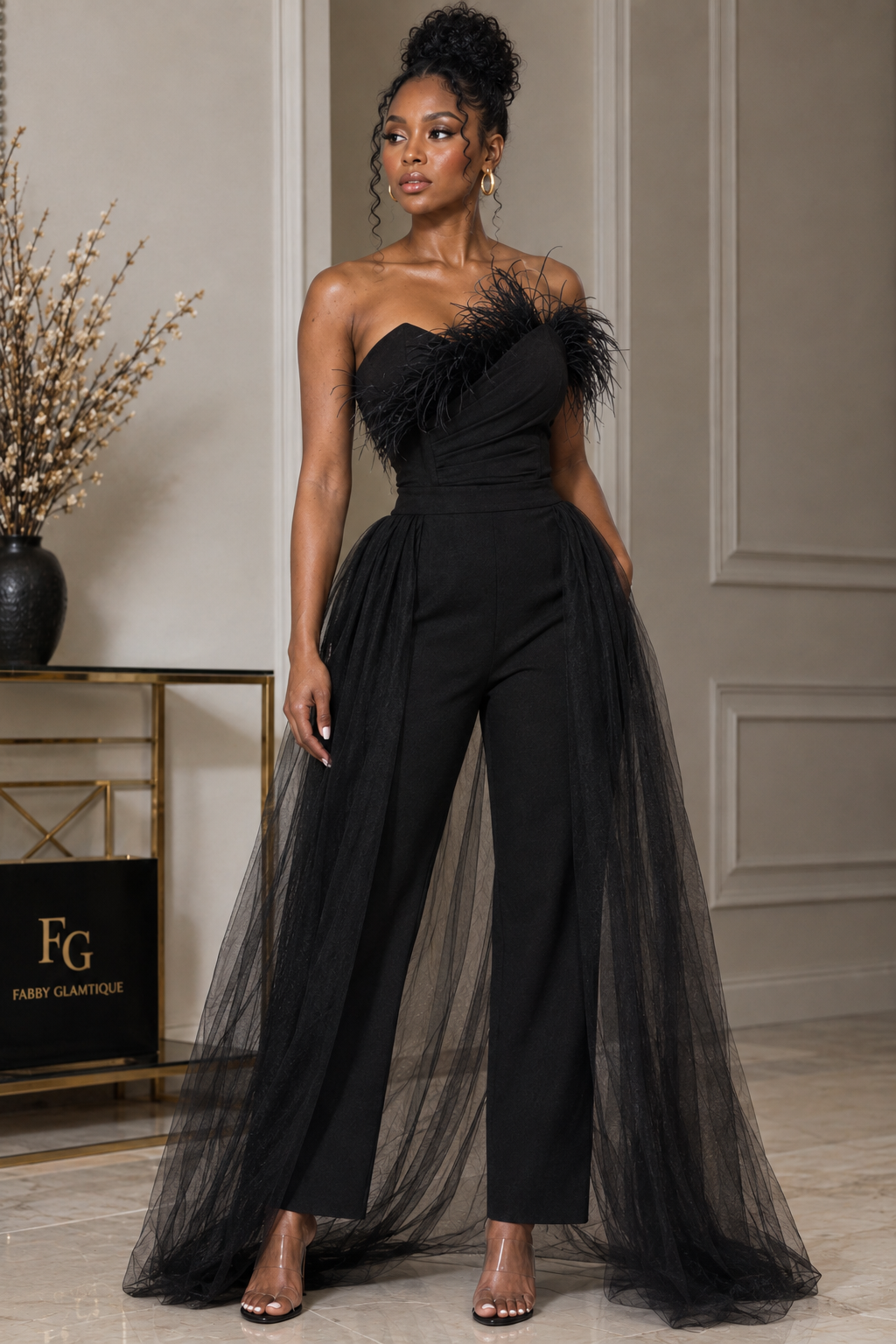 Front view of black strapless jumpsuit with feather-style neckline trim and floor-length sheer overskirt