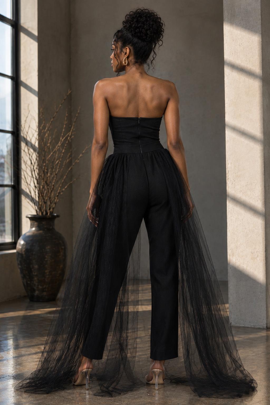 Back view of black strapless jumpsuit with center-back zipper and flowing sheer overskirt
