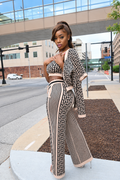 A woman models a matching two-piece outfit featuring a beige and black geometric pattern, consisting of a cropped long-sleeve top and wide-leg pants, set against an urban street background.
